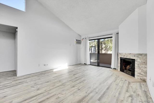 unfurnished living room with a textured ceiling, a wall mounted AC, high vaulted ceiling, light hardwood / wood-style flooring, and a fireplace