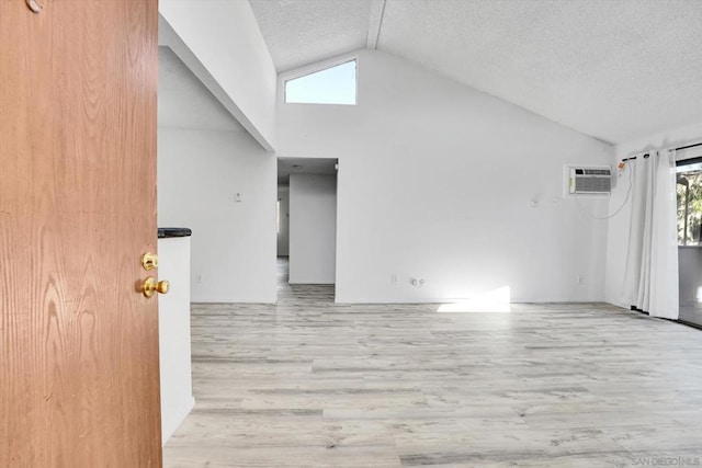 unfurnished living room featuring a wall unit AC, light hardwood / wood-style flooring, high vaulted ceiling, and a textured ceiling