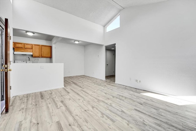 unfurnished living room with sink, a textured ceiling, high vaulted ceiling, and light hardwood / wood-style flooring