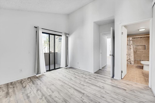 spare room featuring a textured ceiling, light hardwood / wood-style floors, and high vaulted ceiling