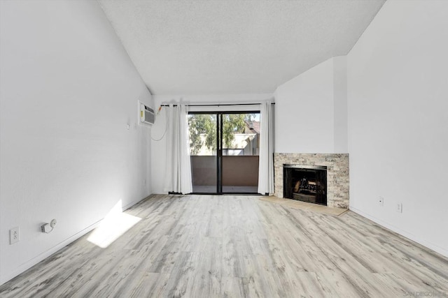 unfurnished living room featuring lofted ceiling, a stone fireplace, light hardwood / wood-style flooring, a textured ceiling, and a wall unit AC