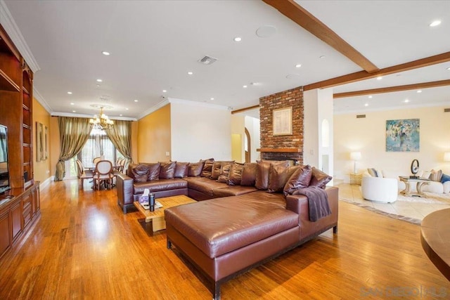 living room featuring a brick fireplace, crown molding, beam ceiling, a chandelier, and light hardwood / wood-style floors