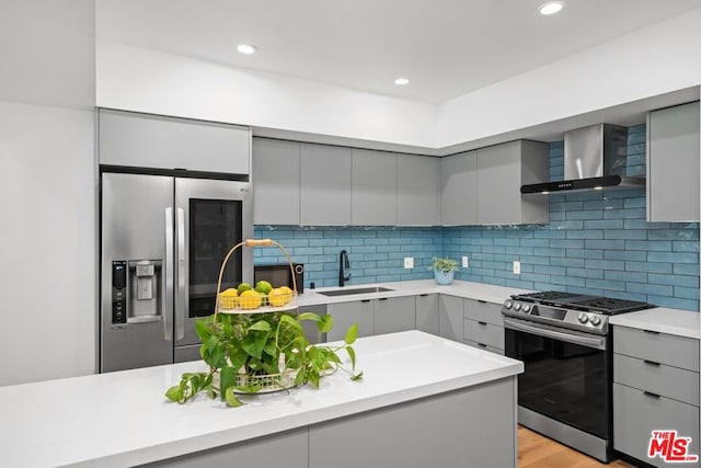 kitchen with appliances with stainless steel finishes, light wood-type flooring, sink, wall chimney range hood, and gray cabinets