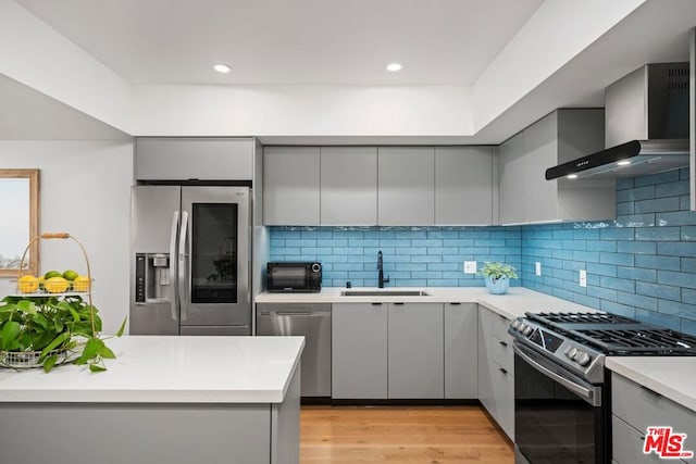 kitchen featuring appliances with stainless steel finishes, gray cabinetry, wall chimney exhaust hood, sink, and light hardwood / wood-style floors