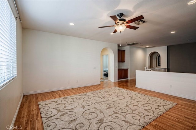 spare room featuring a ceiling fan, visible vents, light wood finished floors, baseboards, and arched walkways