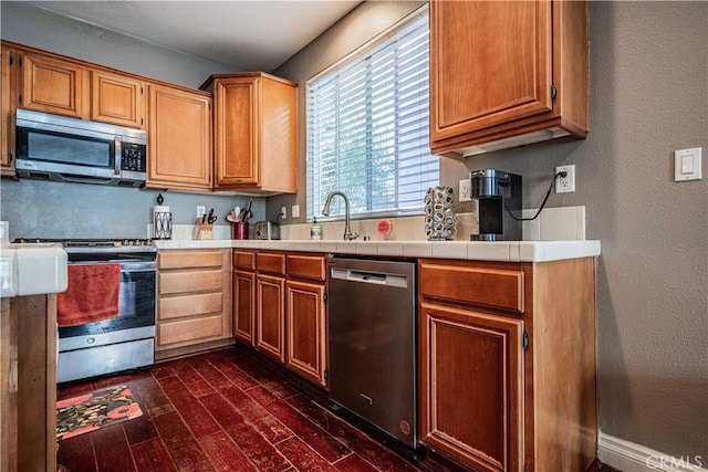 kitchen featuring a sink, a textured wall, dark wood-style flooring, and stainless steel appliances