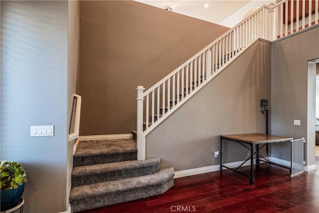 stairway with baseboards, wood-type flooring, and a high ceiling