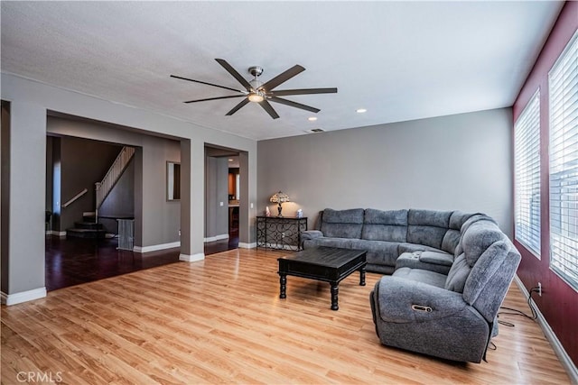 living area with baseboards, a ceiling fan, stairs, and light wood finished floors