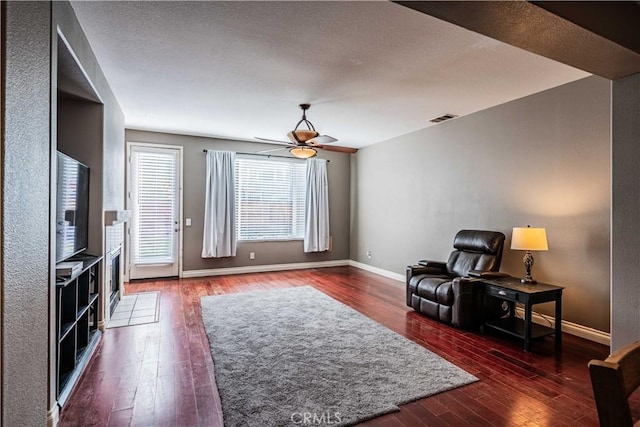 sitting room with dark wood-style floors, visible vents, baseboards, and a ceiling fan