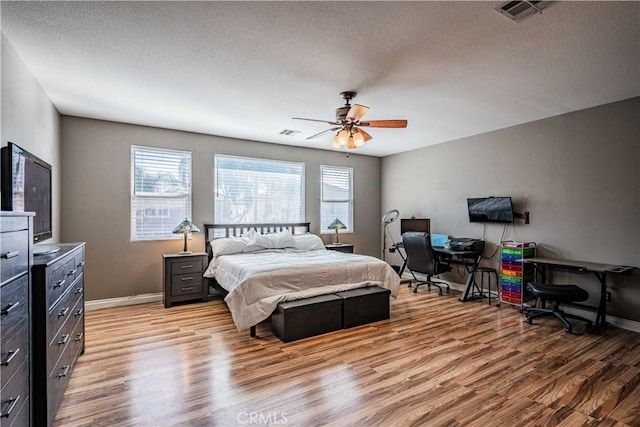 bedroom featuring baseboards, visible vents, light wood finished floors, and a textured ceiling