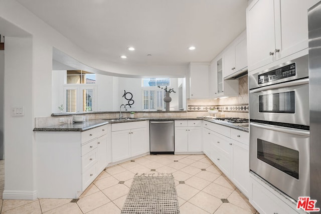 kitchen with sink, backsplash, dark stone countertops, white cabinets, and appliances with stainless steel finishes