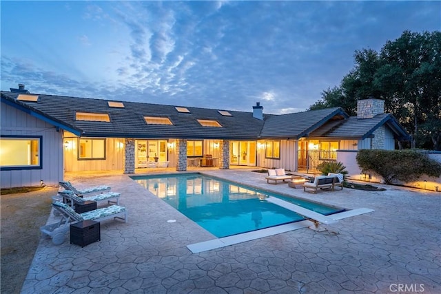 pool at dusk with a patio area, an outdoor pool, a fire pit, and a diving board