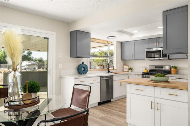 kitchen with gray cabinetry, a raised ceiling, sink, light wood-type flooring, and appliances with stainless steel finishes