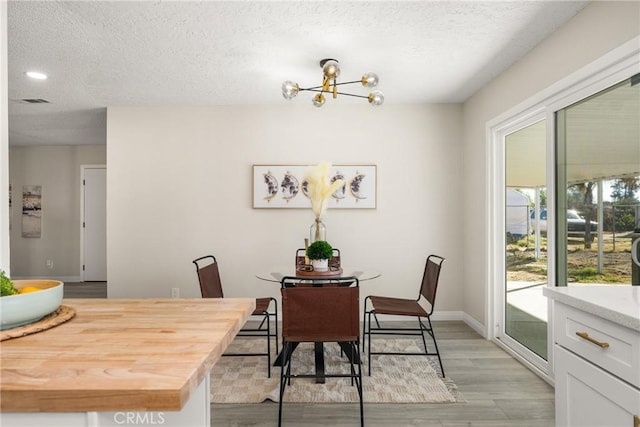 dining space with light hardwood / wood-style flooring, a textured ceiling, and an inviting chandelier