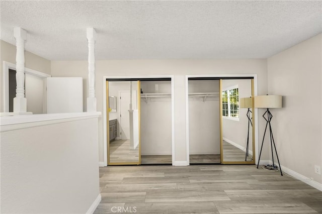 unfurnished bedroom with light hardwood / wood-style floors, a textured ceiling, and two closets