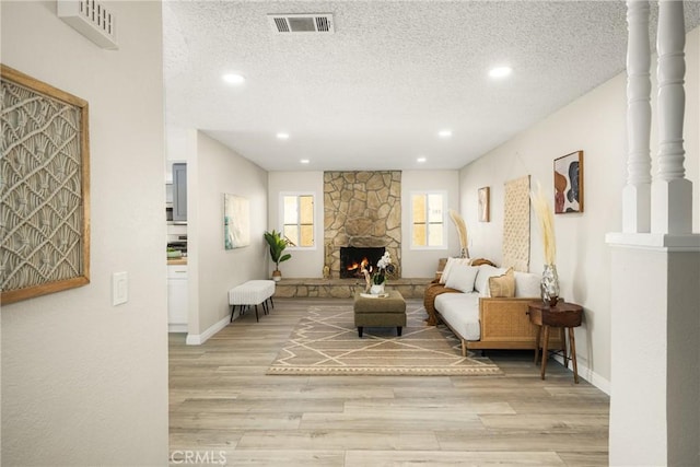 living room featuring a stone fireplace, a textured ceiling, and light hardwood / wood-style flooring