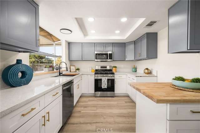 kitchen featuring stainless steel appliances, a raised ceiling, sink, light hardwood / wood-style flooring, and butcher block countertops