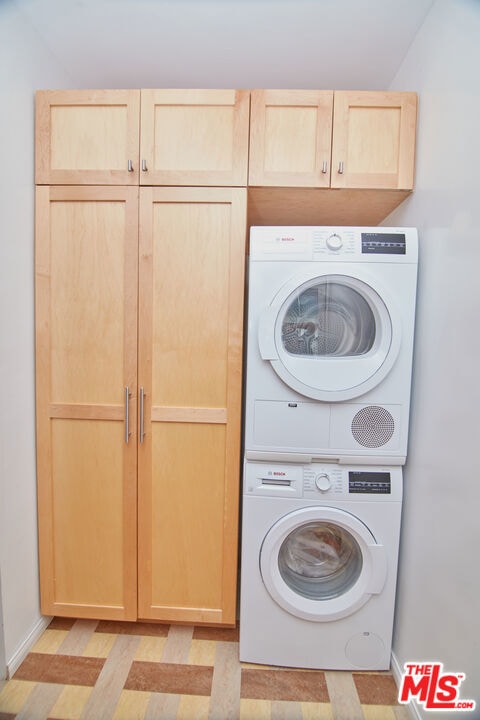 laundry room with stacked washing maching and dryer and cabinets