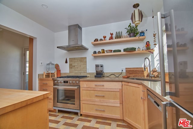 kitchen featuring wall chimney exhaust hood, wooden counters, stainless steel appliances, light brown cabinetry, and sink