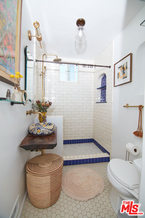 bathroom with toilet, a tile shower, and tile patterned floors