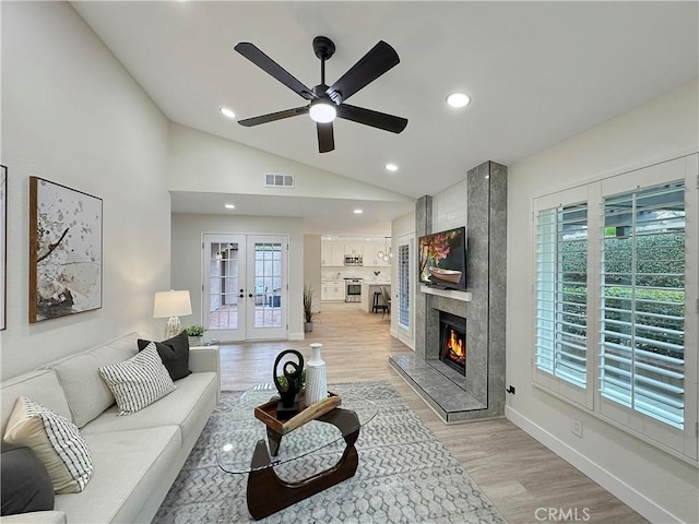 living room with ceiling fan, a large fireplace, french doors, light hardwood / wood-style floors, and vaulted ceiling