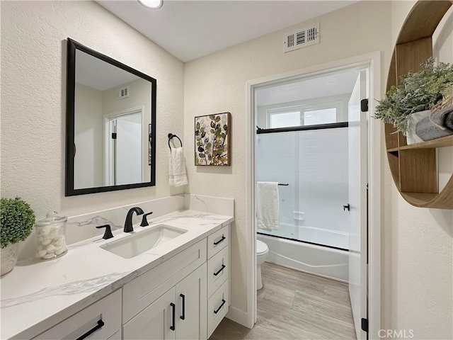 full bathroom featuring shower / bath combination with glass door, wood-type flooring, vanity, and toilet