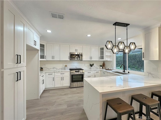 kitchen with kitchen peninsula, appliances with stainless steel finishes, pendant lighting, white cabinetry, and a breakfast bar area