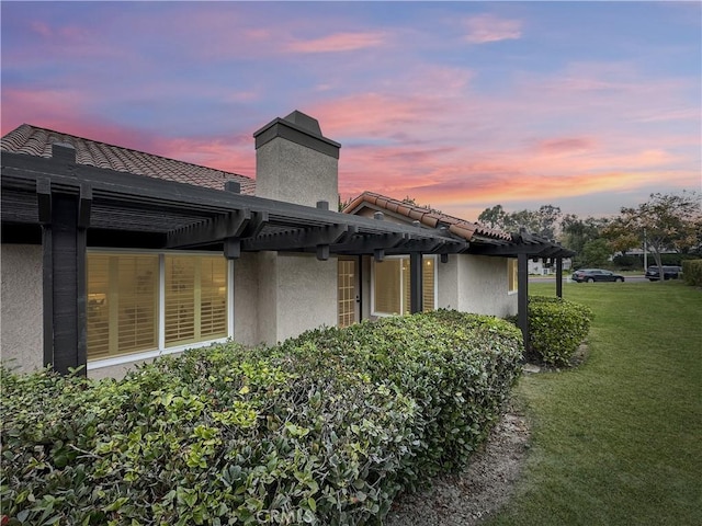 back house at dusk featuring a pergola and a yard