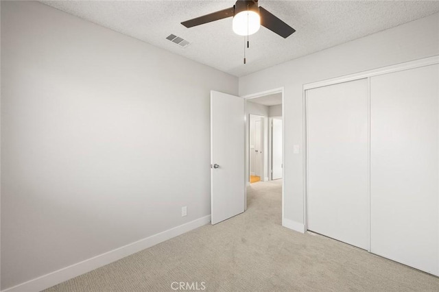 unfurnished bedroom with ceiling fan, light colored carpet, a textured ceiling, and a closet