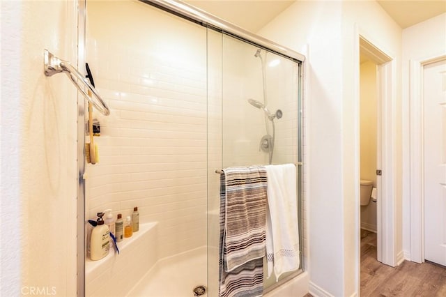 bathroom with wood-type flooring, a shower with shower door, and toilet