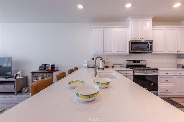 kitchen featuring sink, white cabinets, a kitchen breakfast bar, stainless steel appliances, and light wood-type flooring