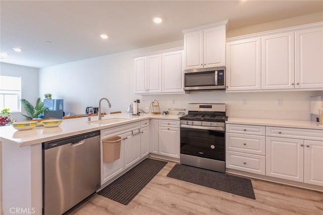 kitchen featuring stainless steel appliances, kitchen peninsula, sink, and white cabinets