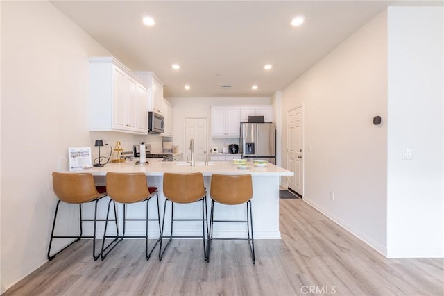 kitchen with a breakfast bar, appliances with stainless steel finishes, kitchen peninsula, and white cabinets