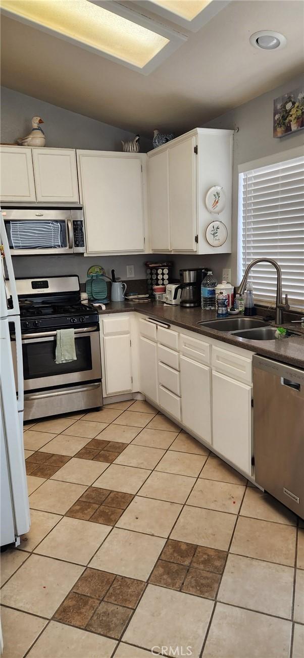 kitchen featuring sink, stainless steel appliances, light tile patterned floors, vaulted ceiling, and white cabinets