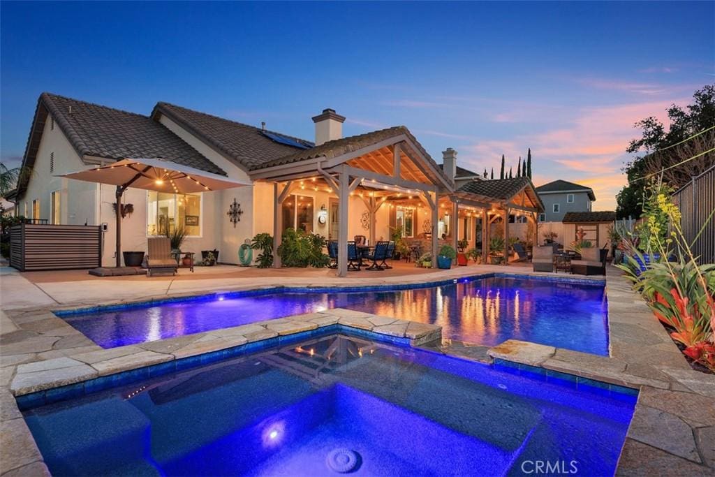 pool at dusk featuring pool water feature, a patio area, and an in ground hot tub