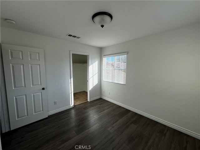 unfurnished bedroom with a spacious closet, a closet, and dark wood-type flooring