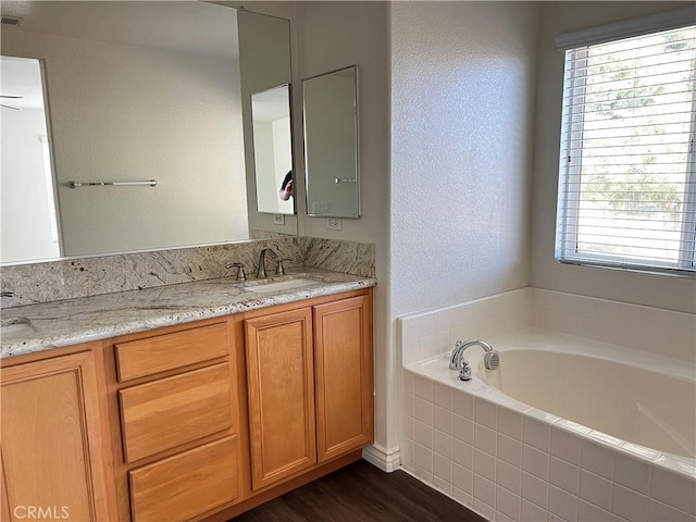 bathroom with plenty of natural light, a relaxing tiled tub, wood-type flooring, and vanity