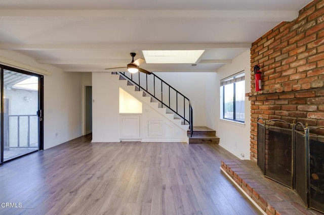 unfurnished living room featuring ceiling fan, a brick fireplace, beamed ceiling, and hardwood / wood-style flooring