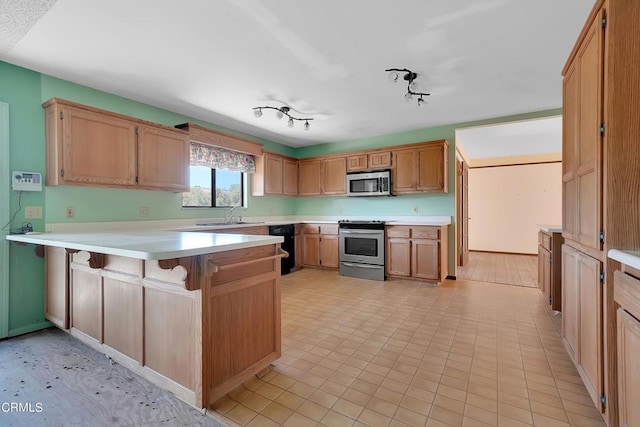 kitchen with kitchen peninsula, a kitchen bar, rail lighting, stainless steel appliances, and sink