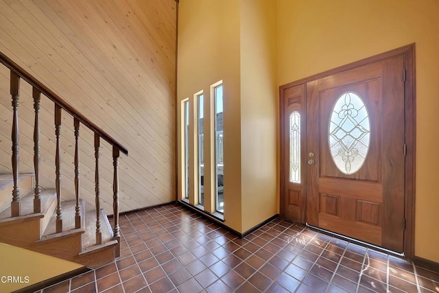 foyer entrance with wooden walls, dark tile patterned flooring, and a high ceiling