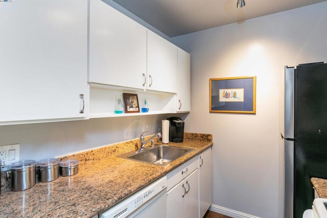 kitchen featuring white dishwasher, sink, stainless steel fridge, light stone countertops, and white cabinetry