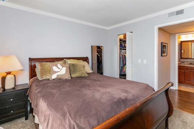 carpeted bedroom with a walk in closet, ornamental molding, and connected bathroom