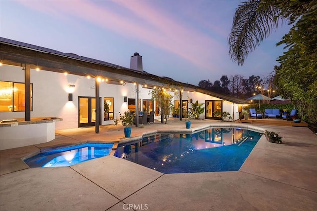 pool at dusk with a jacuzzi and a patio