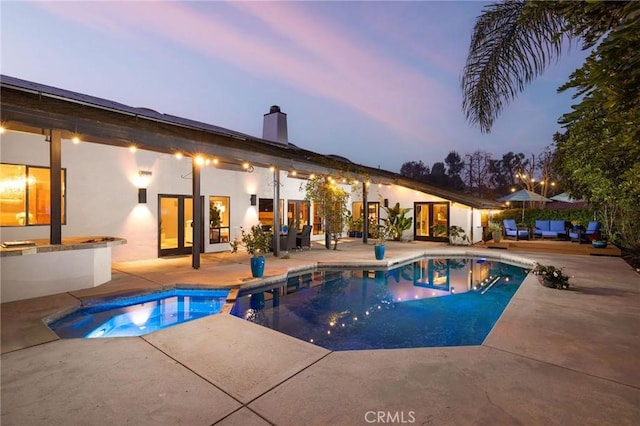 pool at dusk featuring a patio and an in ground hot tub