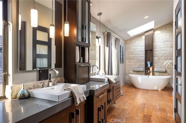 bathroom featuring lofted ceiling with skylight, a tub to relax in, wood-type flooring, and vanity