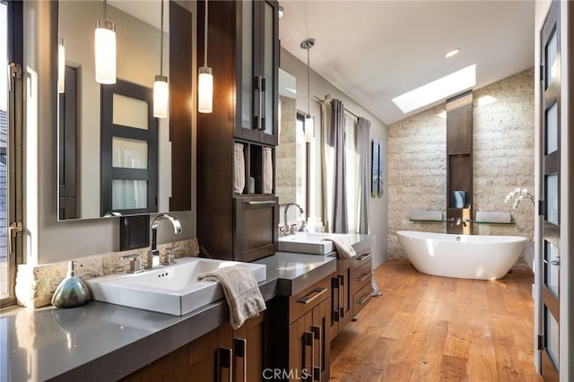 bathroom with hardwood / wood-style flooring, vanity, a tub, and vaulted ceiling with skylight