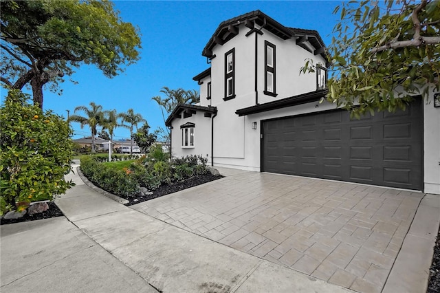 view of side of property featuring an attached garage, decorative driveway, and stucco siding