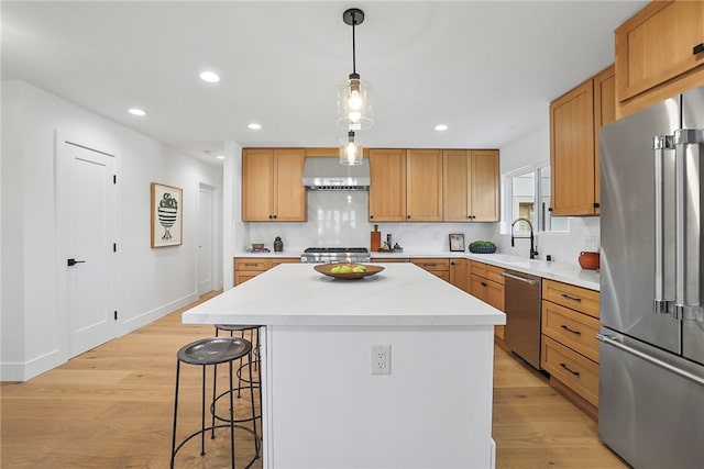 kitchen featuring stainless steel appliances, wall chimney exhaust hood, light wood-style flooring, and a center island