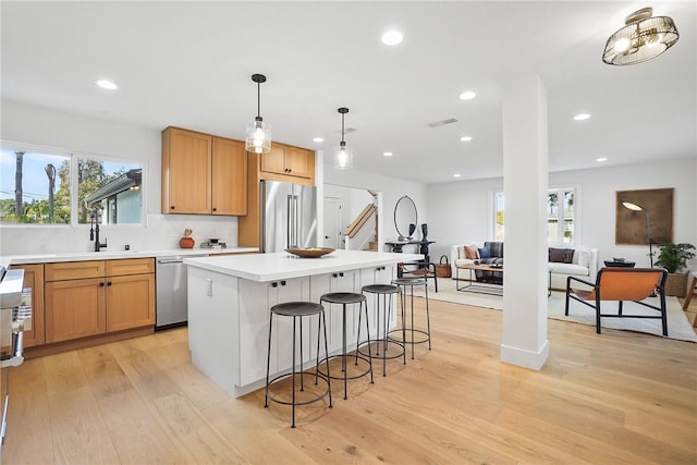 kitchen with a center island, light wood-style flooring, appliances with stainless steel finishes, a sink, and a kitchen bar