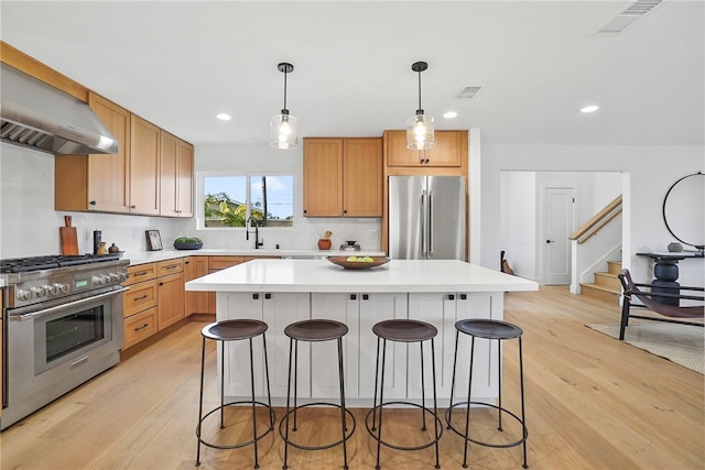 kitchen featuring a breakfast bar, visible vents, appliances with stainless steel finishes, light wood-type flooring, and wall chimney exhaust hood